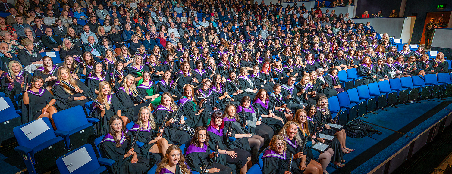 Graduates in robes holding scrolls sitting in an audience
